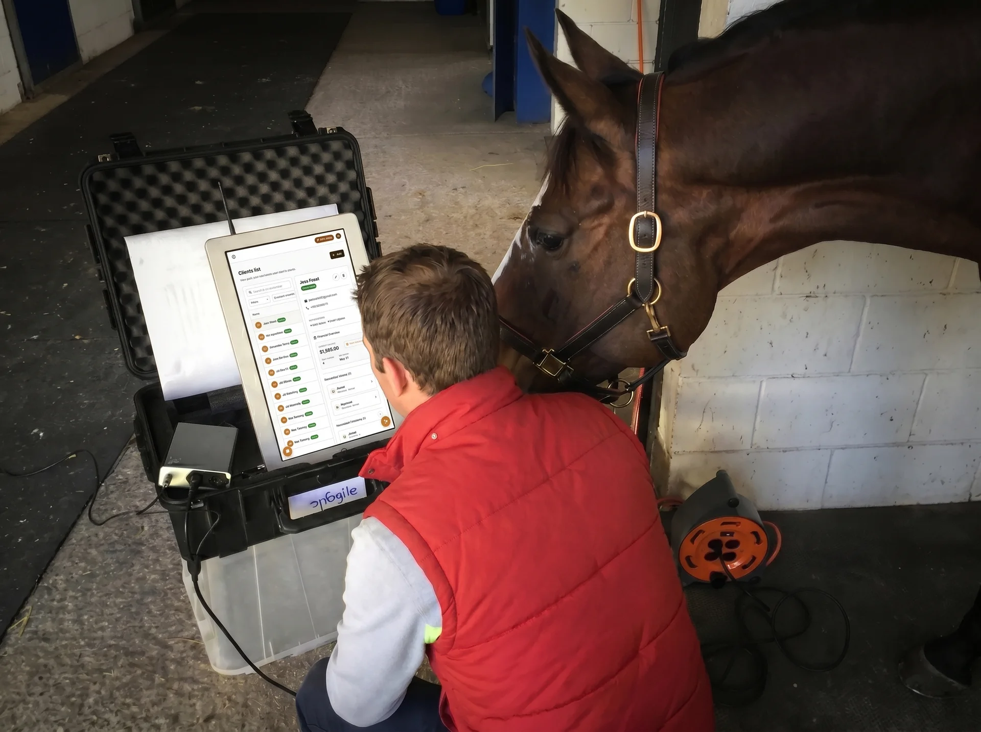 Equine veterinarian using StableTrack practice management software on a rugged field tablet beside a horse in a barn aisle